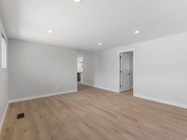 Spacious room featuring wood-finish flooring, light grey walls, white baseboards, recessed lighting, and a window for natural illumination