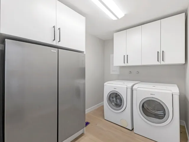 Utility area featuring a side-by-side refrigerator, white cabinetry with contemporary hardware, and wood-finish flooring