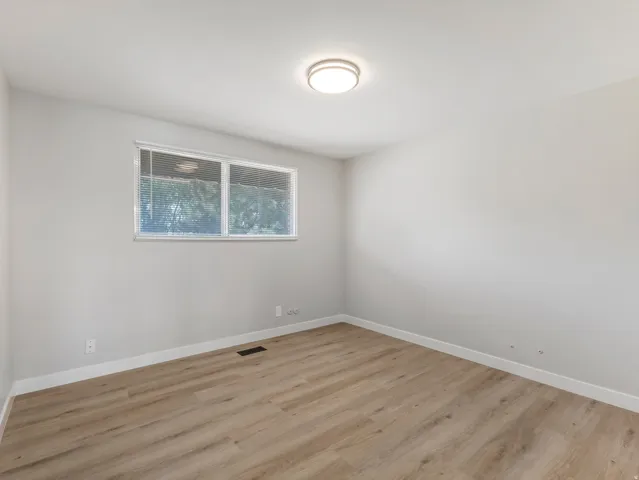 Bright interior space featuring light wood-finish flooring, a contemporary flush-mount ceiling light, white baseboards, and a double-pane window with blinds