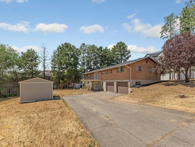 Brick exterior home featuring a concrete driveway, two car garage, upper-level balcony, and a separate storage shed