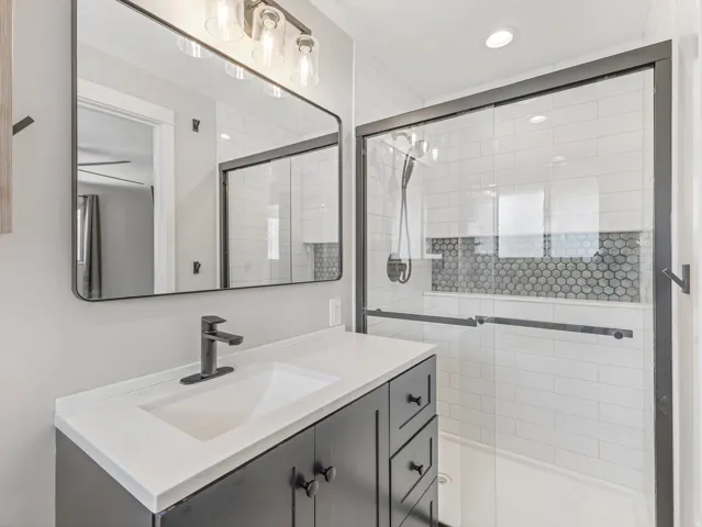 Bathroom featuring a dark wood-finish vanity with a white countertop and integrated sink, a rectangular mirror, and a glass-enclosed shower with subway tile and penny tile accents