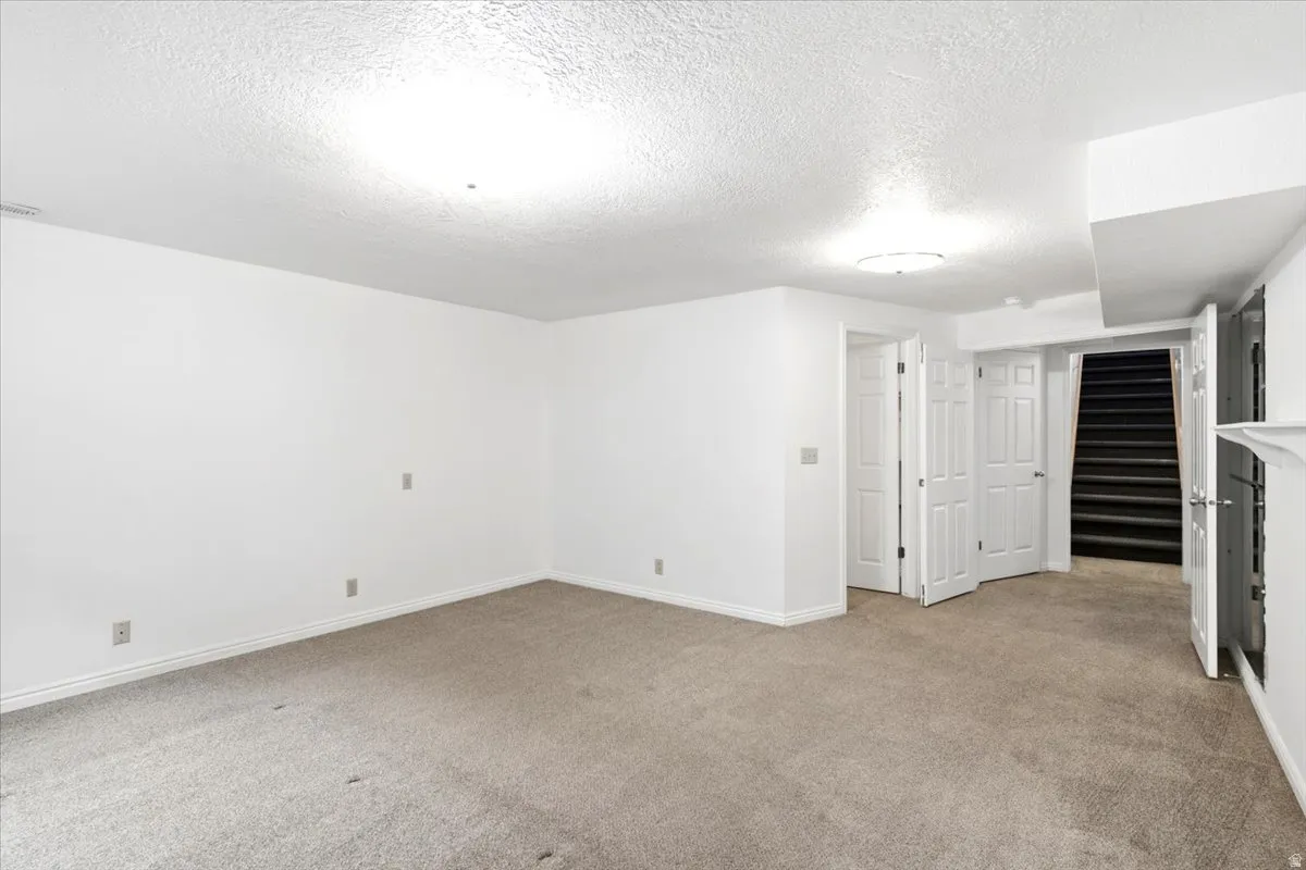 Spacious room featuring neutral carpeting, white walls, multiple access doors, and a staircase