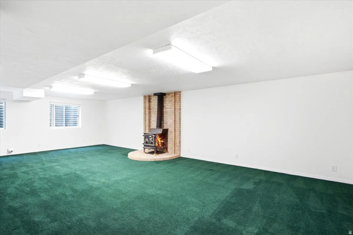 Spacious room featuring a central wood-burning stove with a brick surround, white walls, and green carpeting