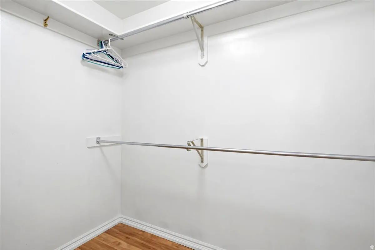 White-painted closet featuring two chrome hanging rods and wood-finish flooring