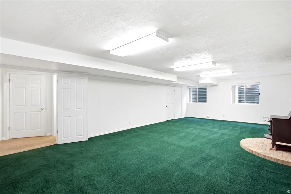 Spacious carpeted room featuring multiple windows with blinds, a brick-base hearth, and fluorescent overhead lighting
