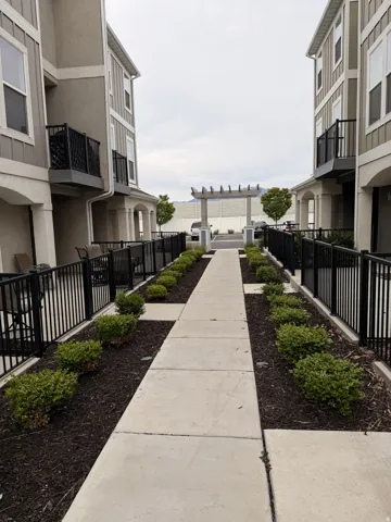 Concrete walkway flanked by manicured shrubs and black metal fencing