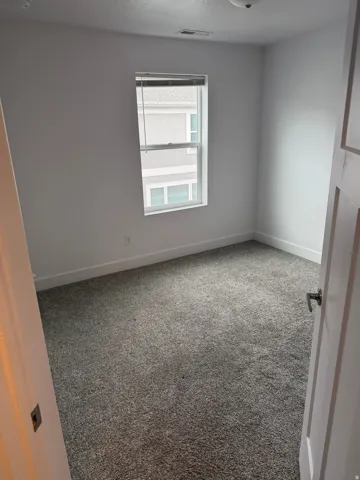 Carpeted room featuring a single window with blinds, white walls, and a white baseboard