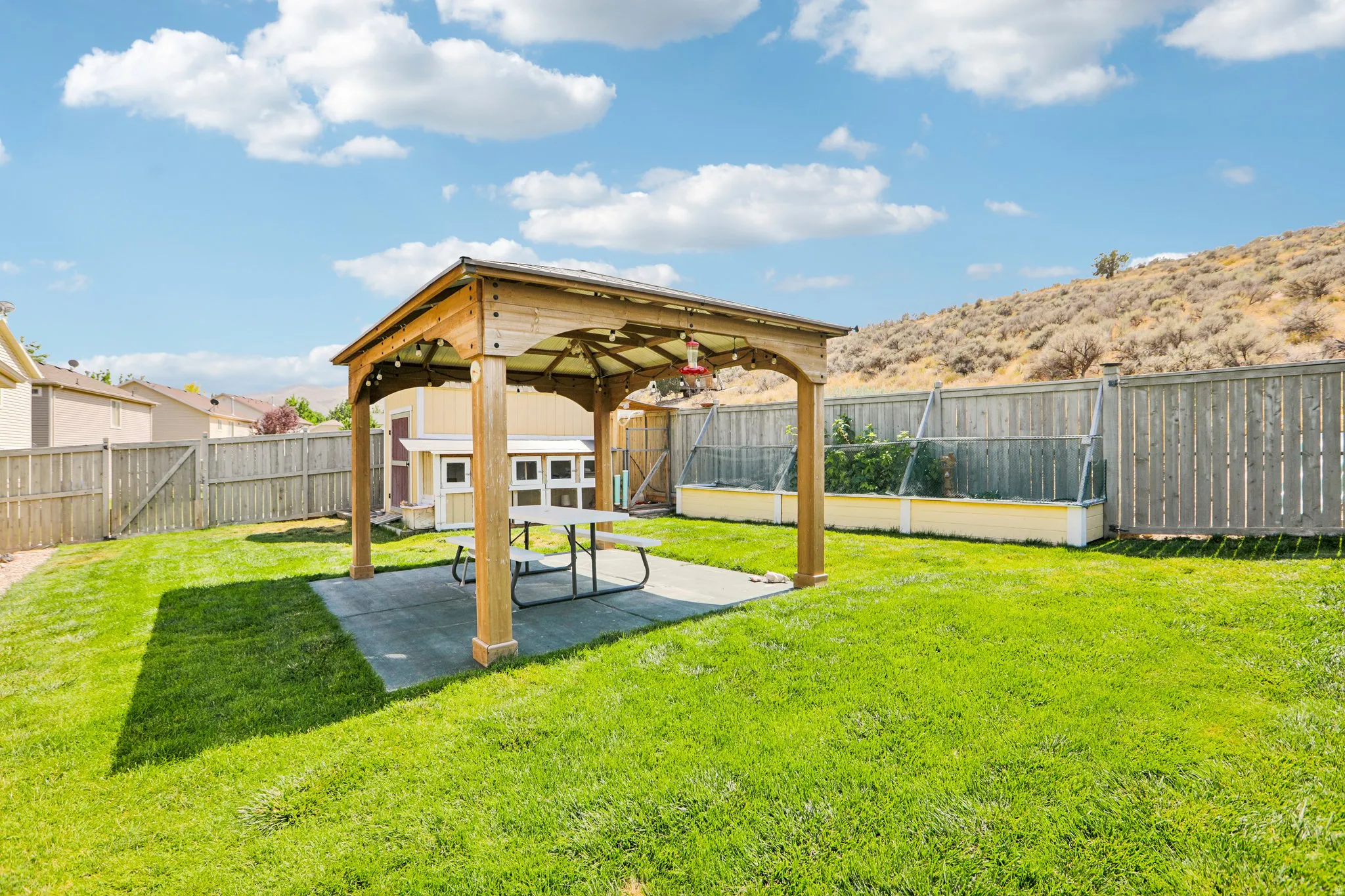 Spacious backyard featuring a wooden gazebo with a concrete pad, raised garden beds, and a fenced perimeter