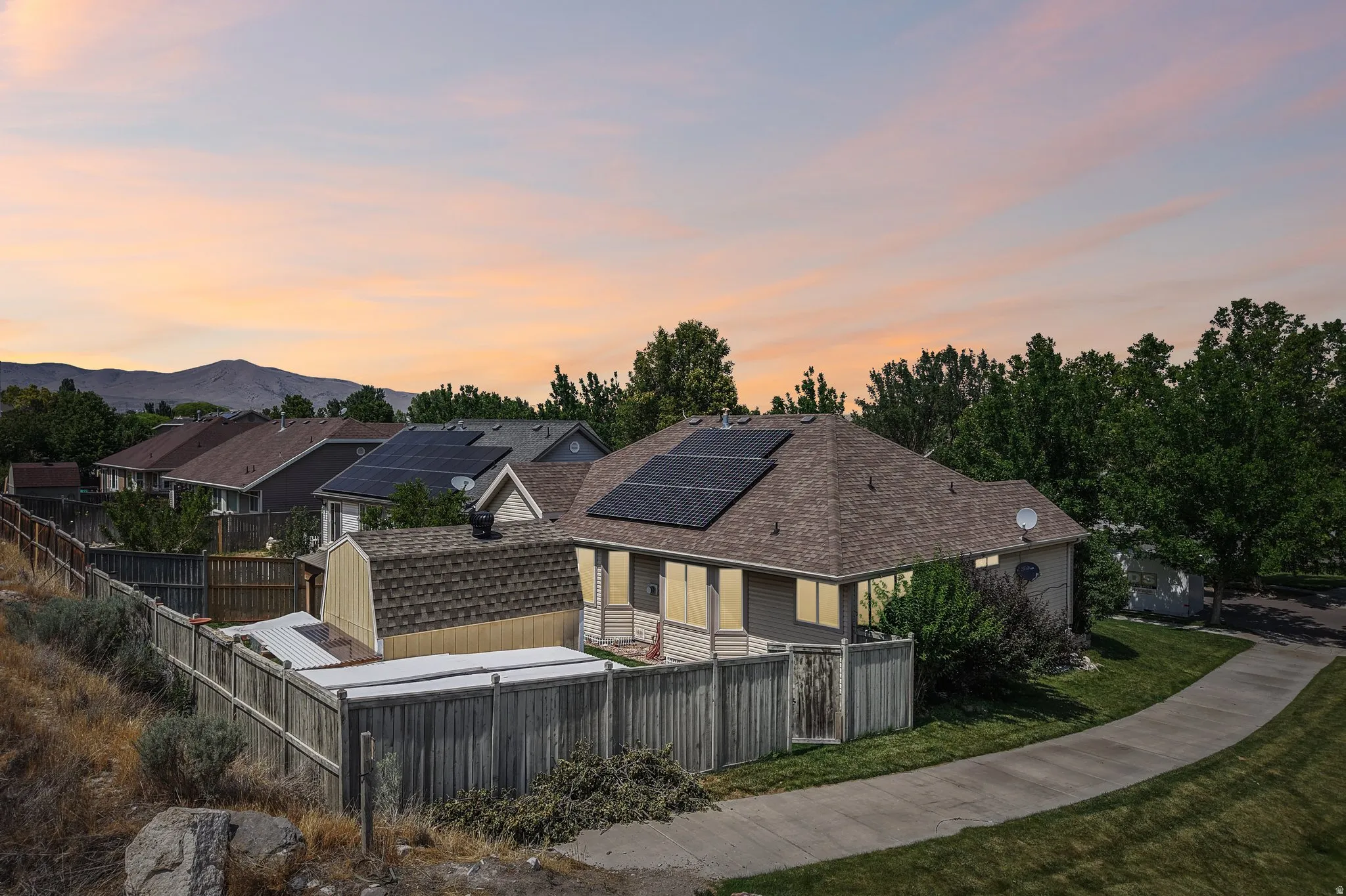 Single-story residence featuring a shingle roof with integrated solar panels, a wooden privacy fence, and a patio area