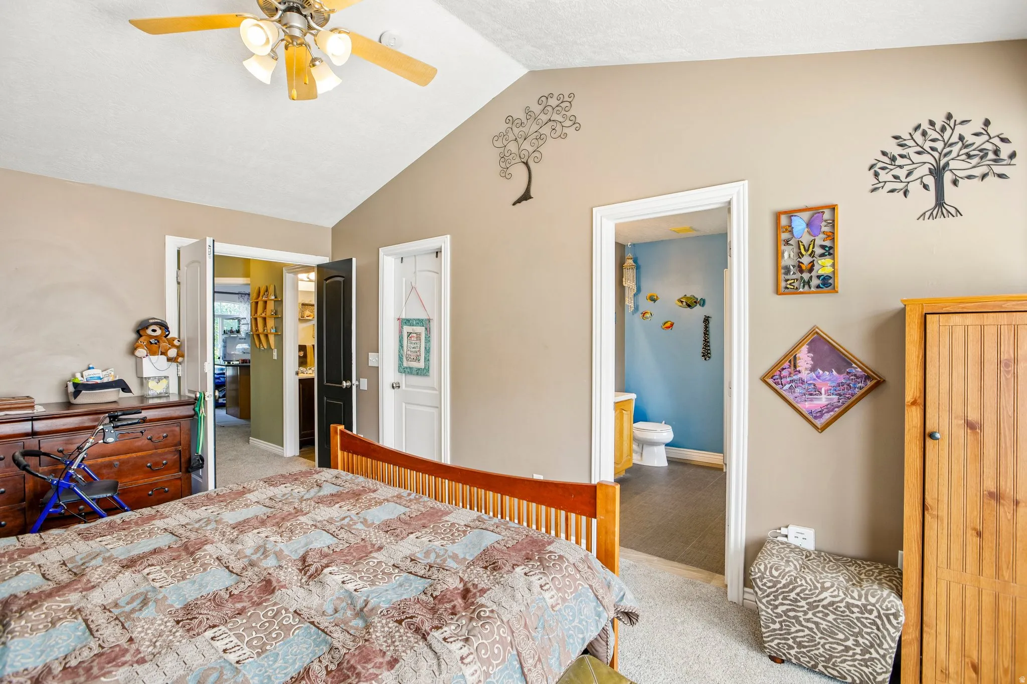 Vaulted ceiling bedroom featuring a ceiling fan with integrated lighting, carpet flooring, and an en-suite bathroom with a built-in vanity and toilet