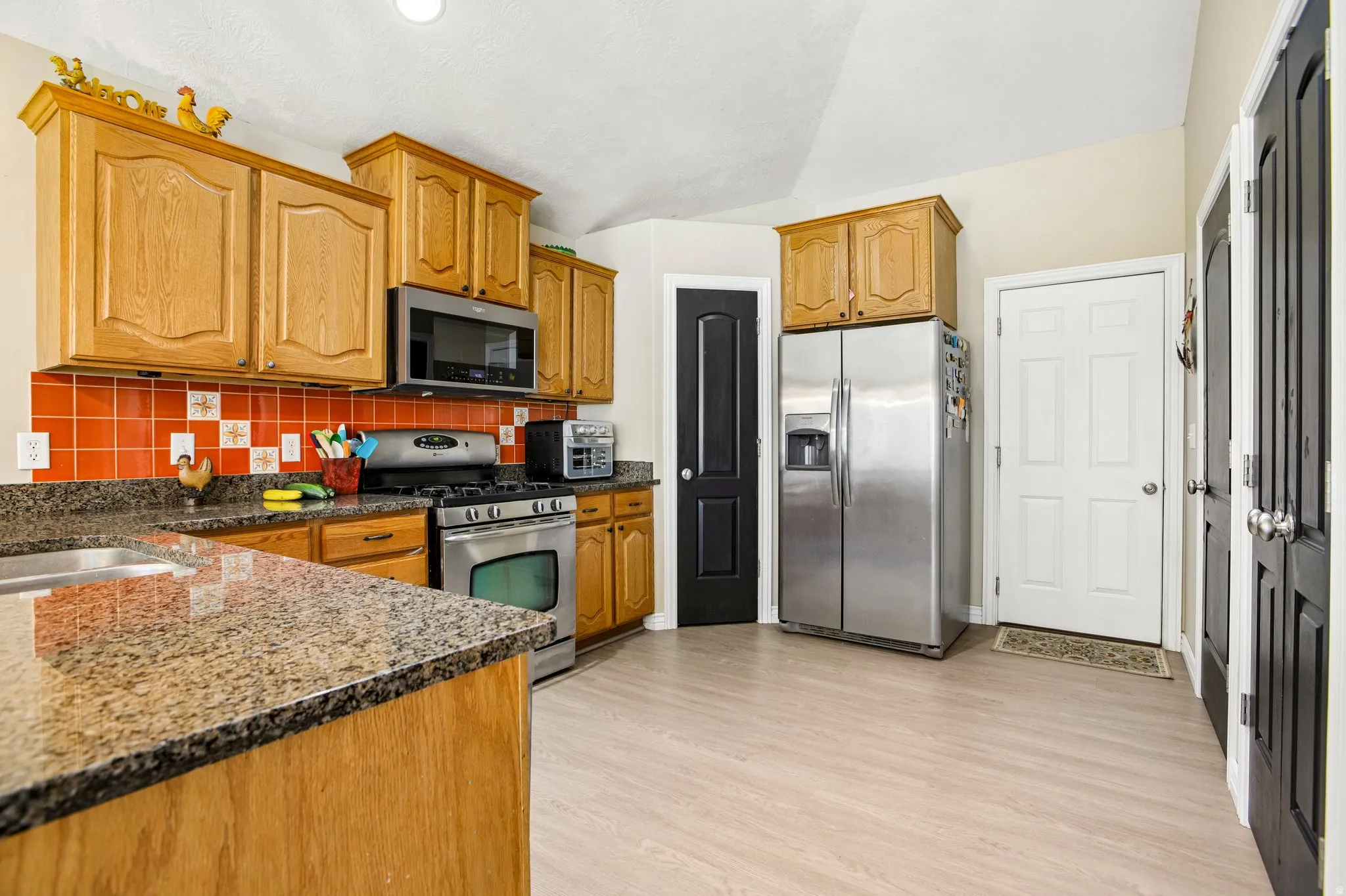 Kitchen featuring light wood cabinetry, stone-look countertops, and a red tile backsplash