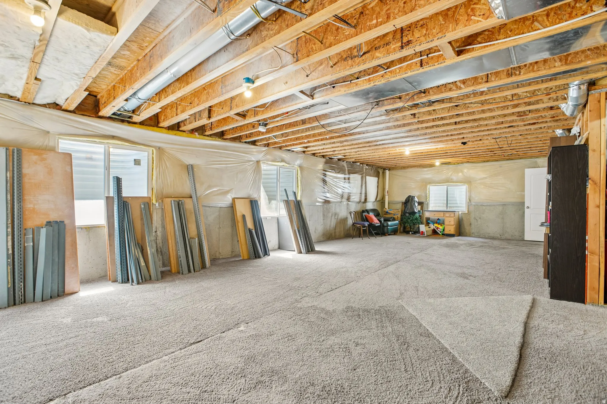 Expansive unfinished lower level with exposed wood joists and ductwork, multiple windows, and light grey carpeting throughout