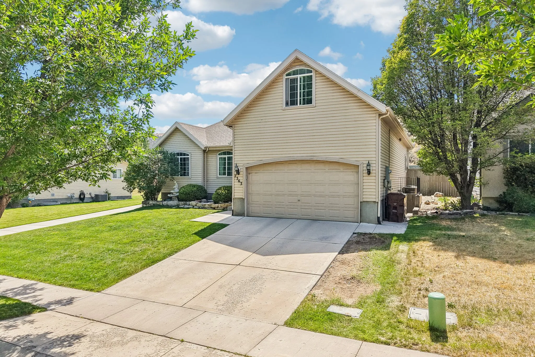 Exterior featuring light-colored siding, a two-car garage, an arched window, and a concrete driveway