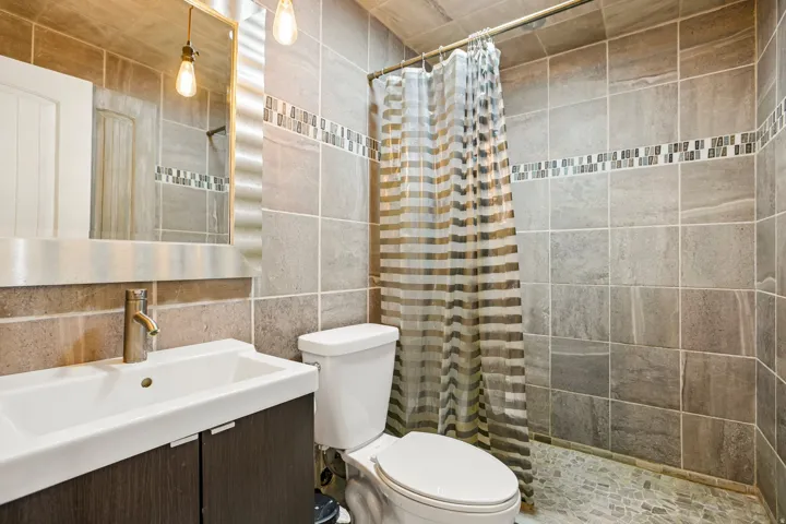 Bathroom featuring floor-to-ceiling tile, a decorative mosaic tile accent band, and a shower area with pebble-finish flooring