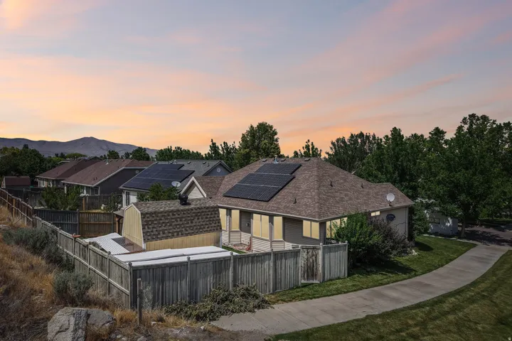 Single-story residence featuring a shingle roof with integrated solar panels, a wooden privacy fence, and a patio area
