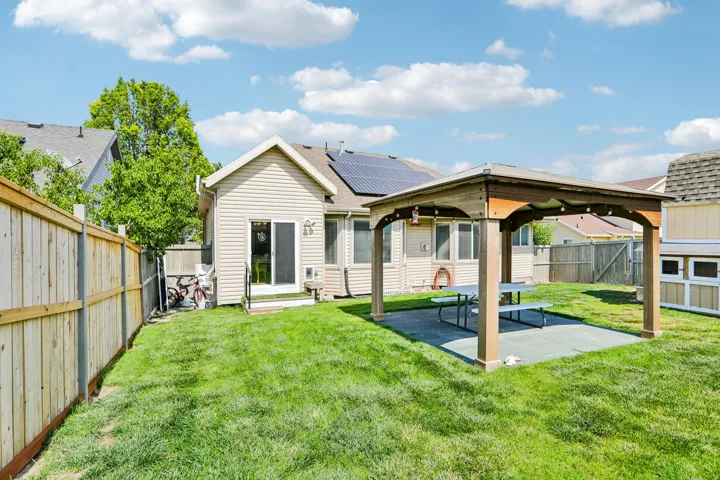 Spacious backyard featuring a covered patio, a wood-panel fence, a sliding glass door, and solar panels on the roof