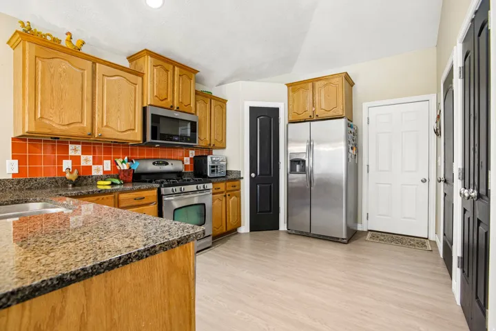 Kitchen featuring light wood cabinetry, stone-look countertops, and a red tile backsplash