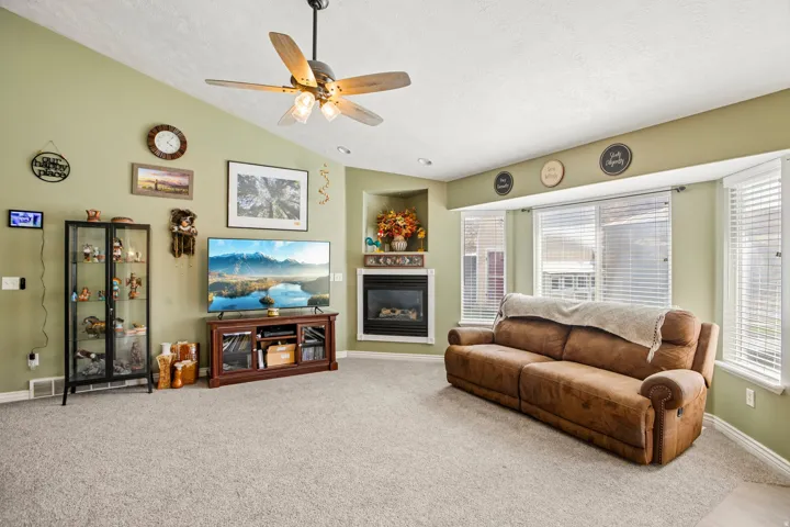 Living area featuring vaulted ceilings, a ceiling fan with integrated lighting, and carpet flooring