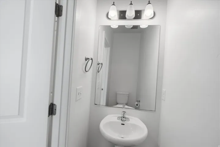 Pedestal sink with a chrome faucet, illuminated by a three-light vanity fixture
