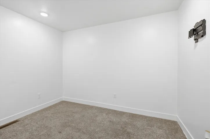 Carpeted room featuring white walls, white baseboards, a recessed ceiling light, and a wall-mounted bracket