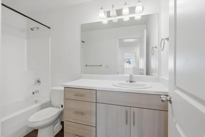 Bathroom featuring a white tub/shower combination, a vanity with a light wood-finish and white countertop, an undermount sink, and a large mirror with overhead lighting