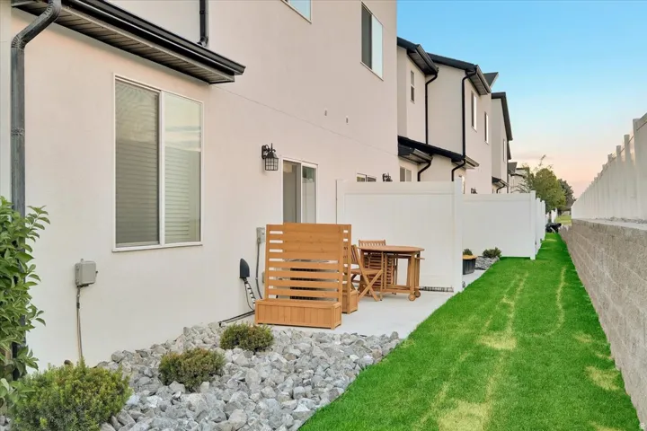 Paved patio area featuring white privacy fencing, a landscaped rock garden, and a strip of green lawn