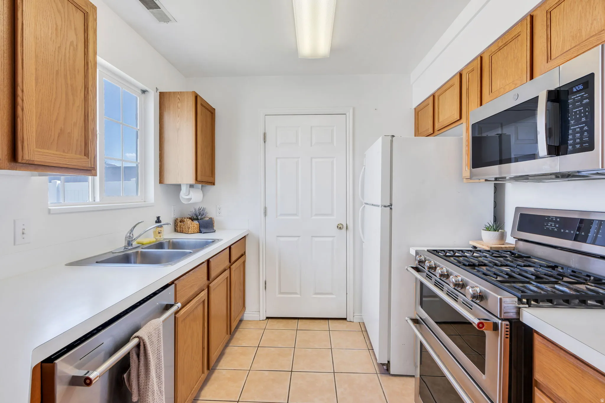 Kitchen featuring warm wood cabinetry, stainless steel appliances, a double basin sink, and tile flooring