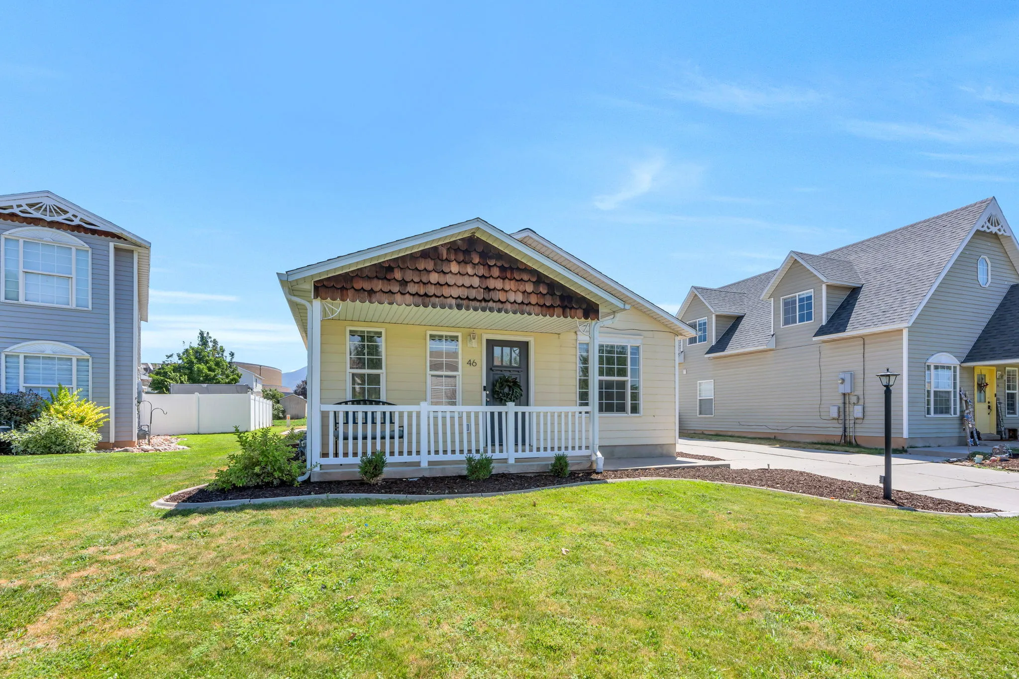 Charming single-story residence featuring yellow siding, a covered front porch with white railing, and a distinctive brown scalloped shingle roof accent