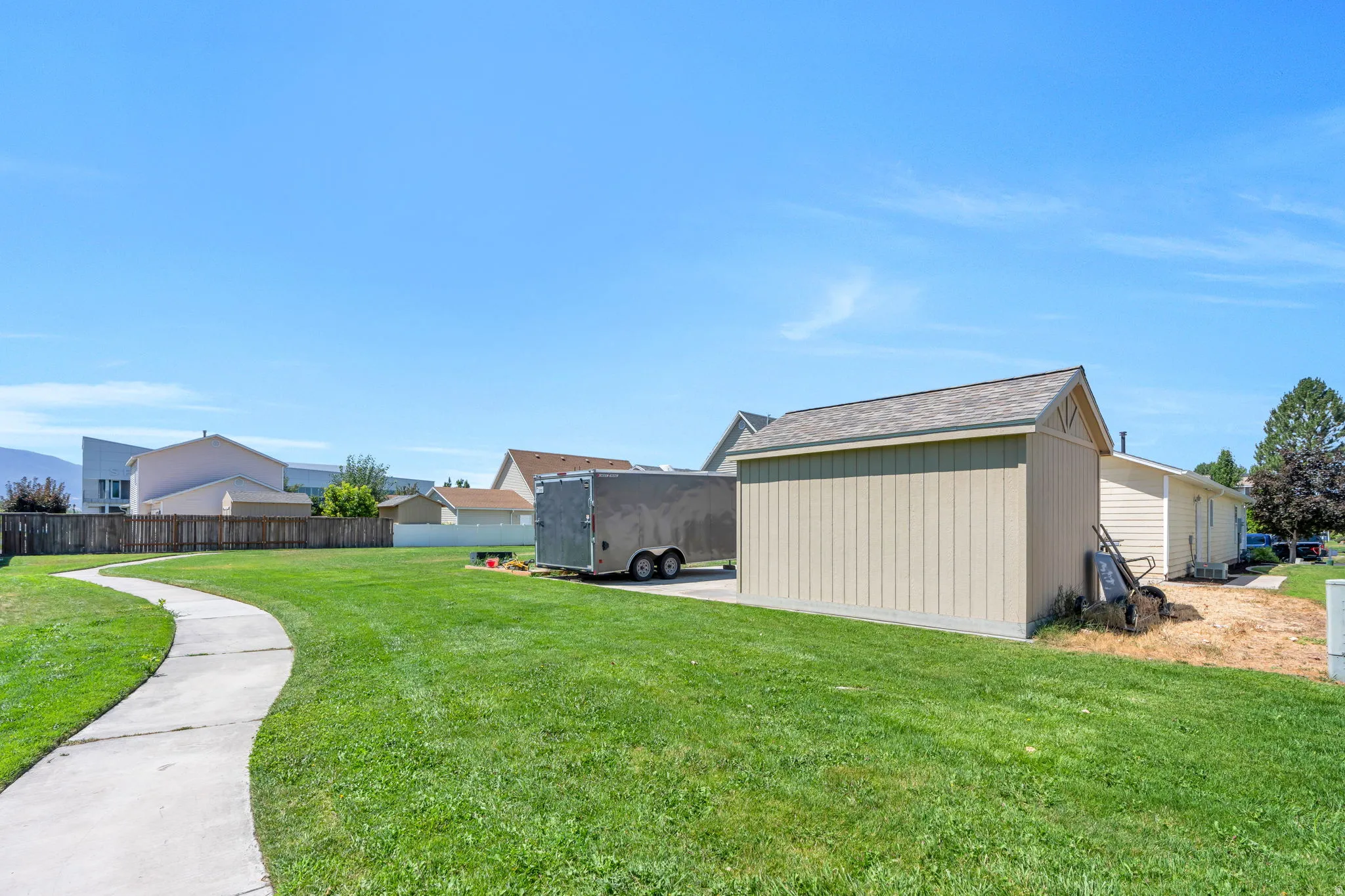 Expansive green lawn with a curved concrete pathway and a detached shed featuring vertical siding and a shingled roof