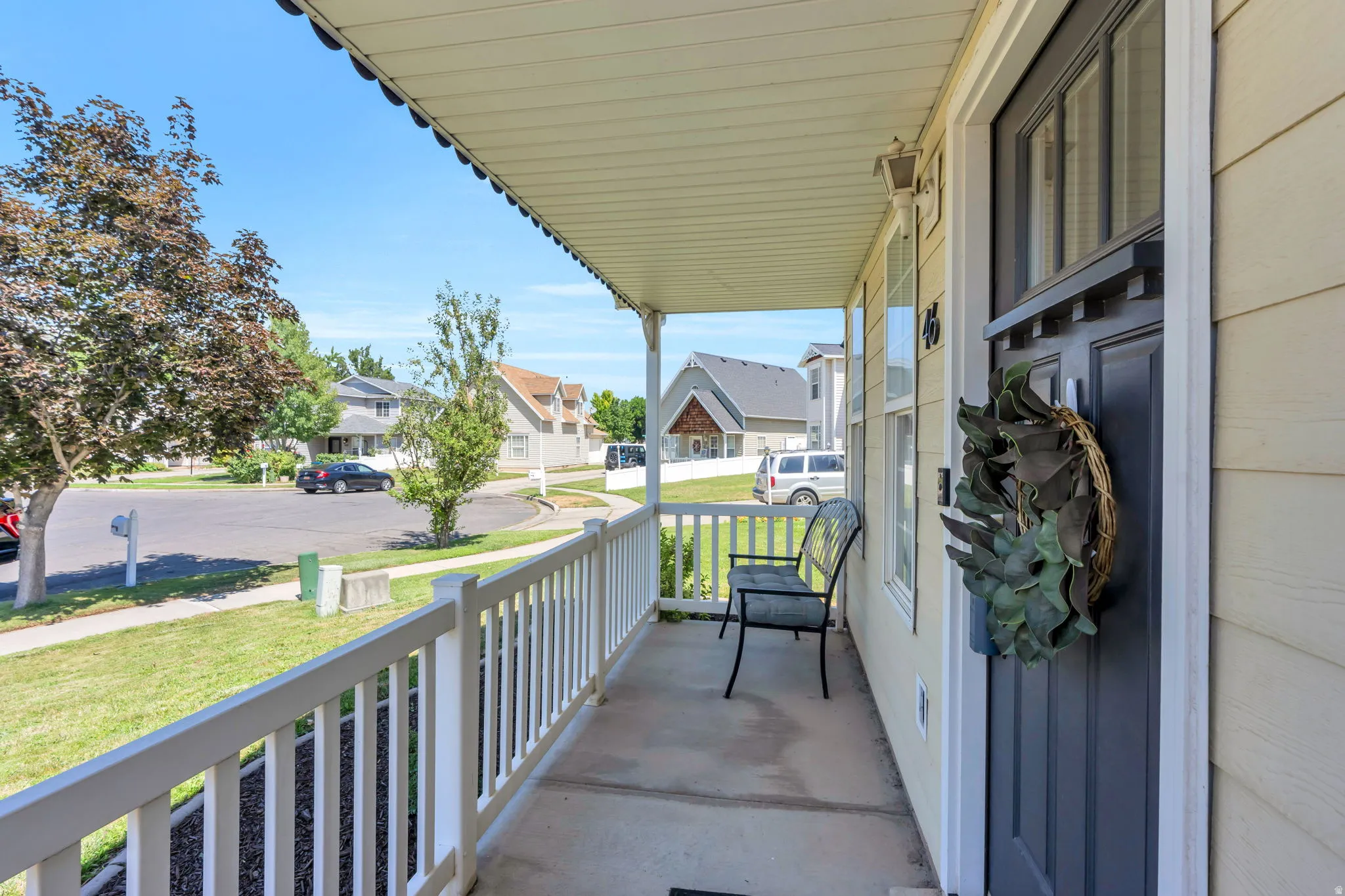 Covered front porch with white railings, light-colored siding, and a dark entry door