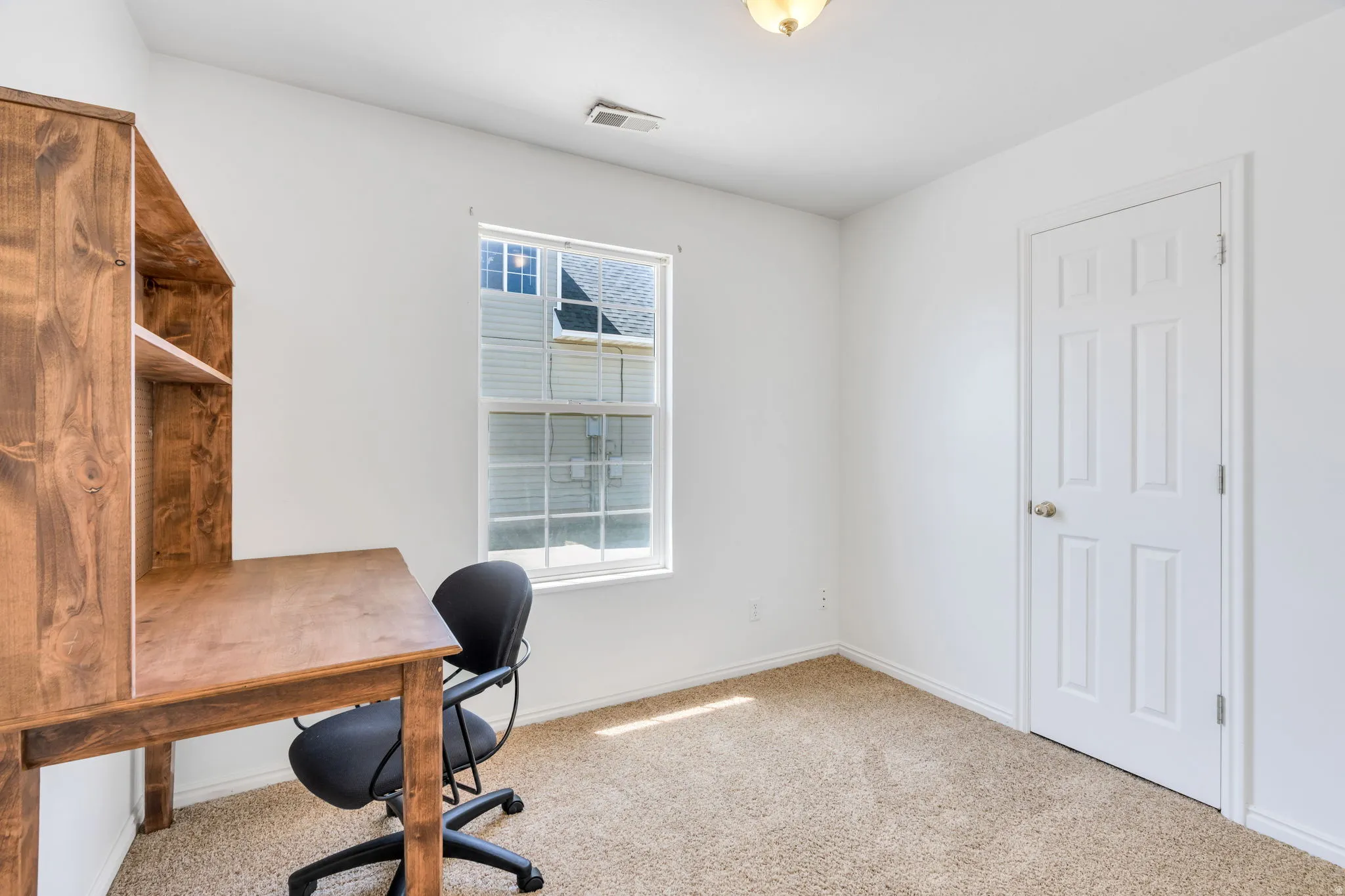 Room with light-toned carpet, a white door with a silver-toned knob, and a window featuring white blinds