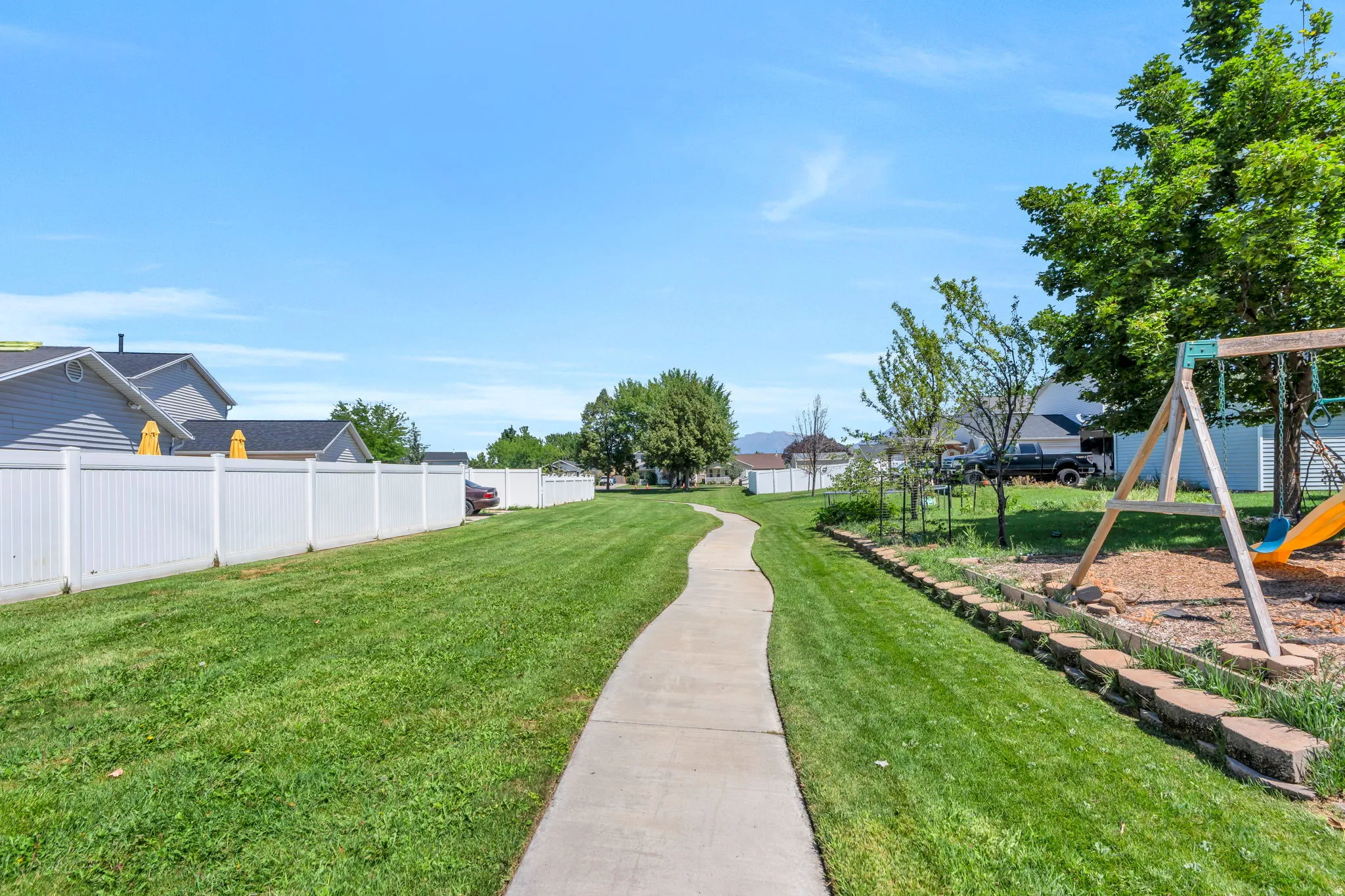 Curved concrete pathway through a spacious lawn, bordered by a white privacy fence