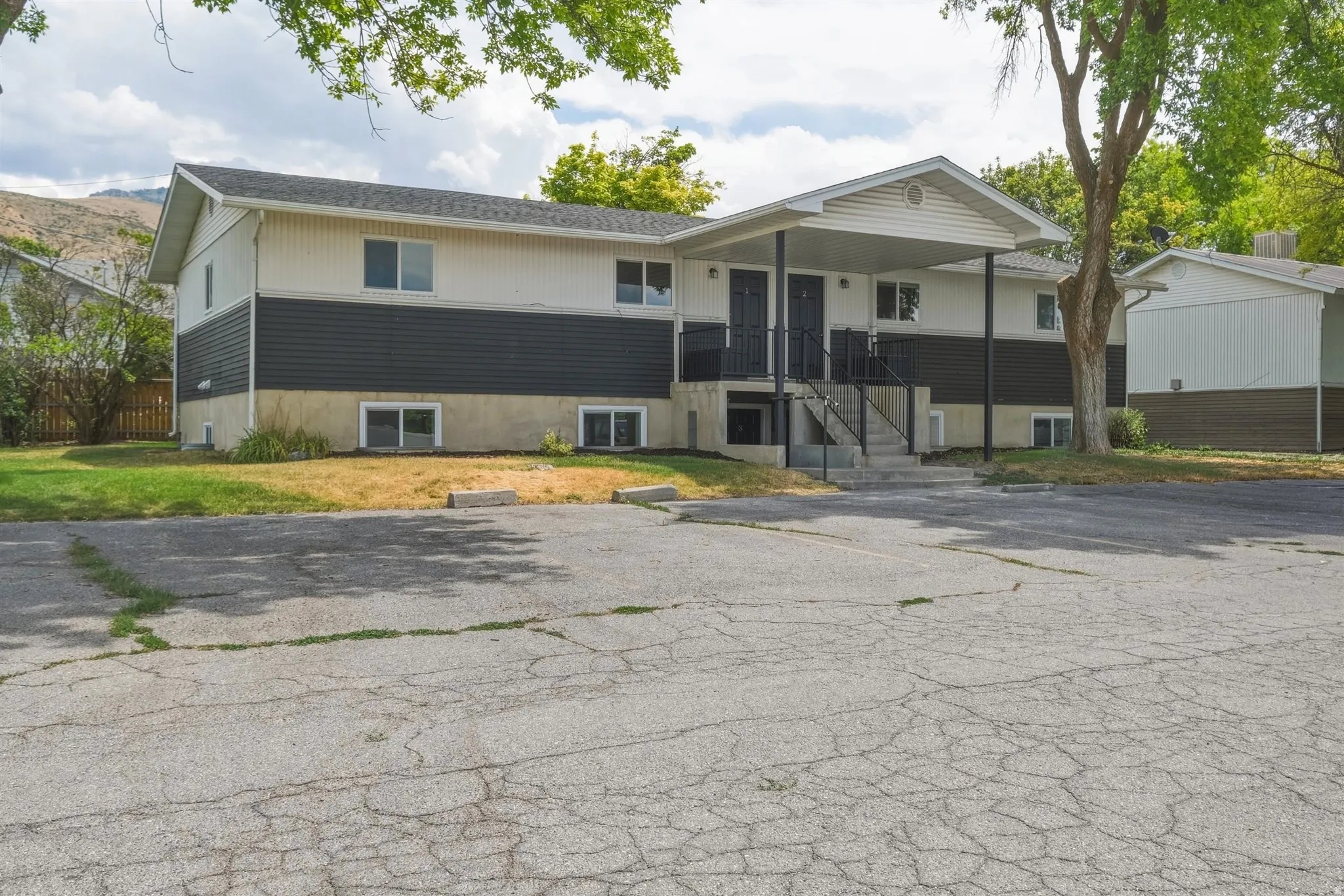 Two-story multi-unit structure featuring a covered entry porch, dark siding accents, and a paved parking area