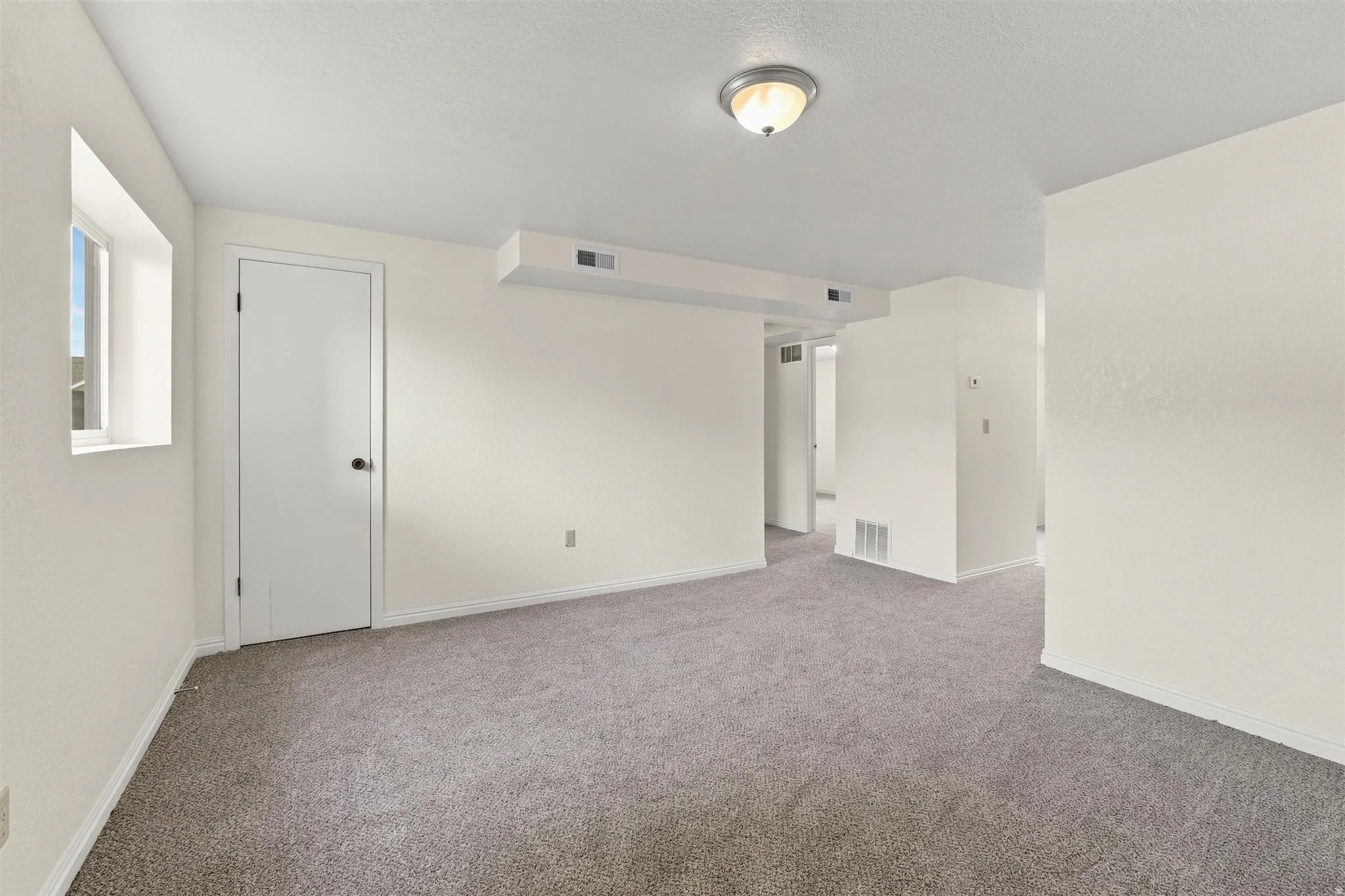 Spacious room featuring gray carpet, light-toned walls, a semi-flush mount ceiling light, and a window providing natural illumination