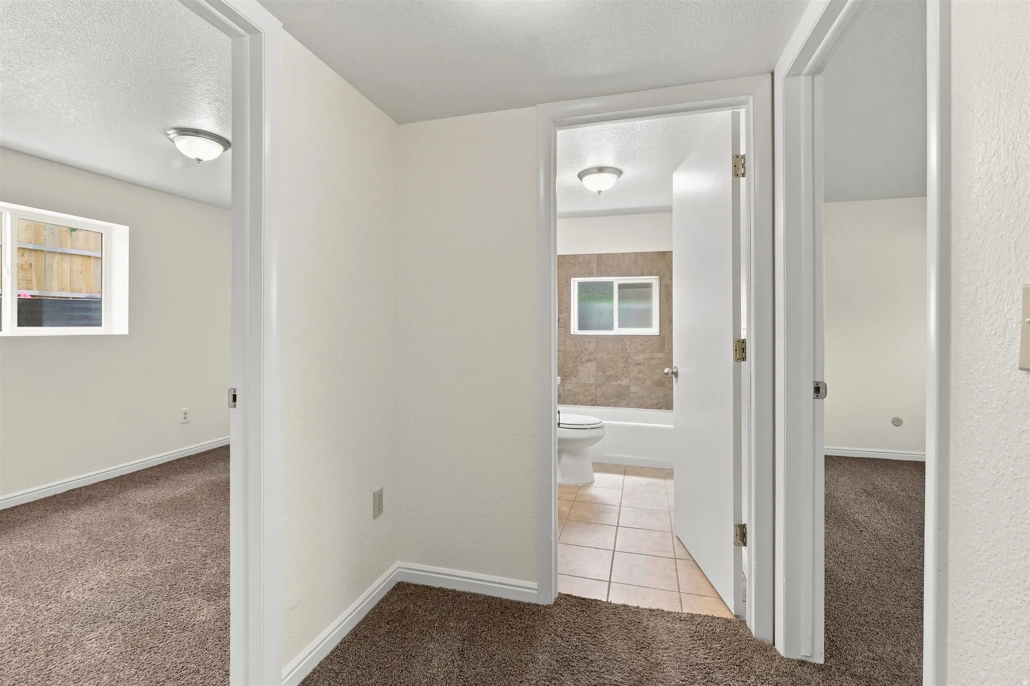 Hallway featuring white walls, textured brown carpeting, and white baseboards