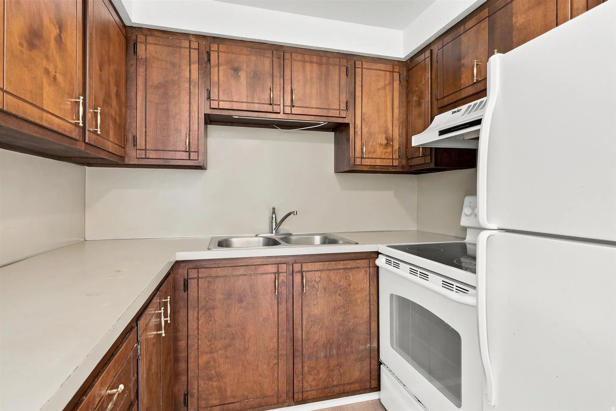 Kitchen featuring ample wood cabinetry, light-toned countertops, a stainless steel double-basin sink, white electric range with hood, and a white refrigerator