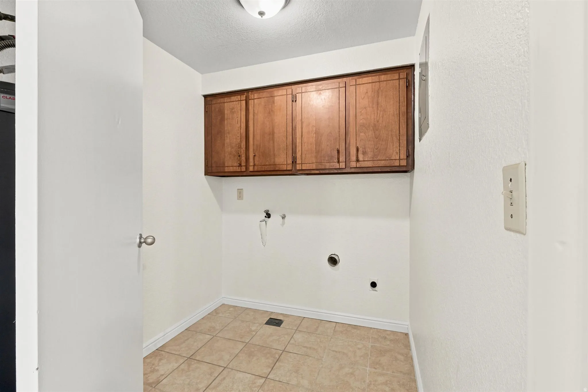 Dedicated utility room featuring ceramic tile flooring, wood-finish cabinetry, and overhead flush-mount lighting