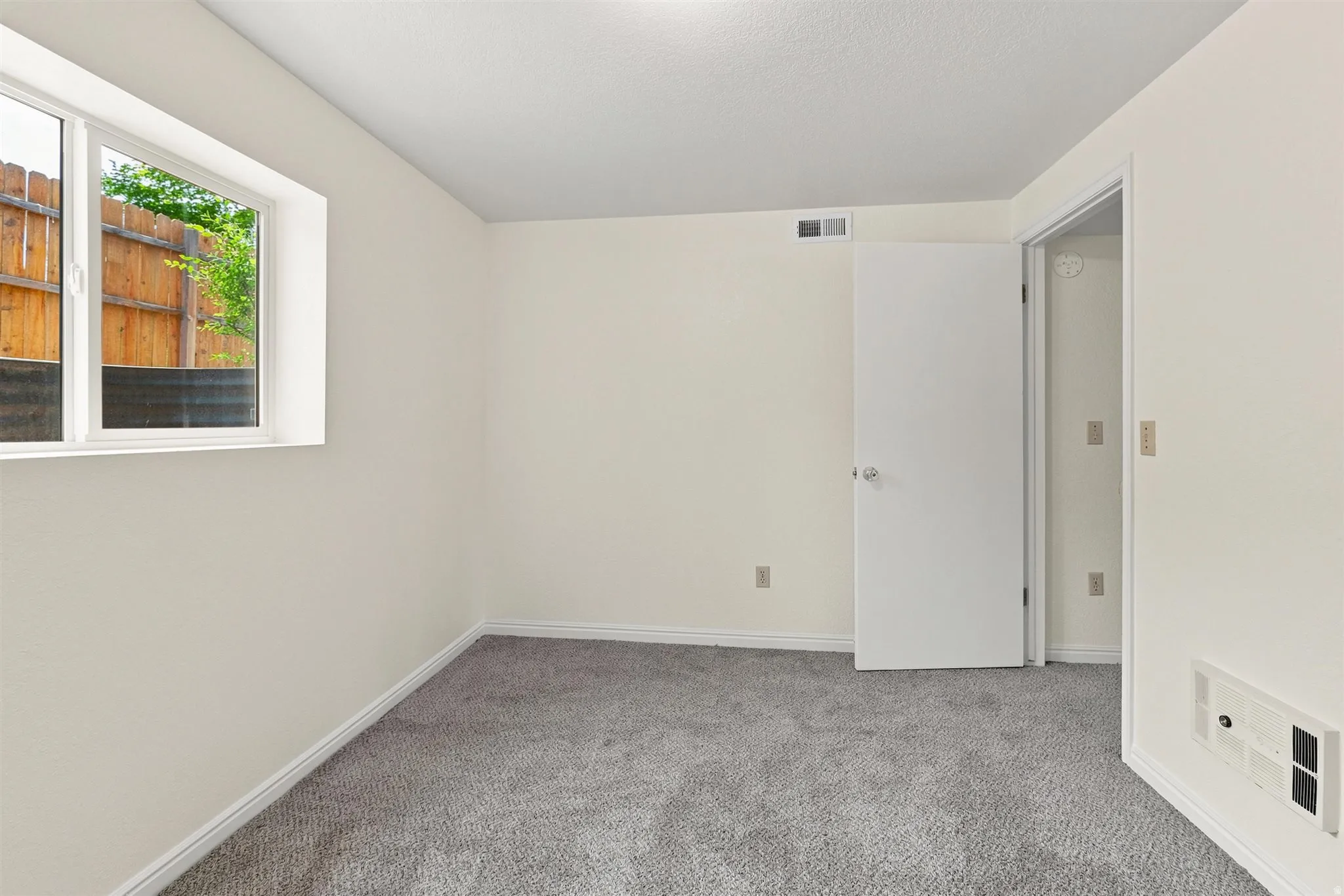 Bright room with neutral wall paint, gray carpet flooring, white trim, a double-pane window, and a white interior door