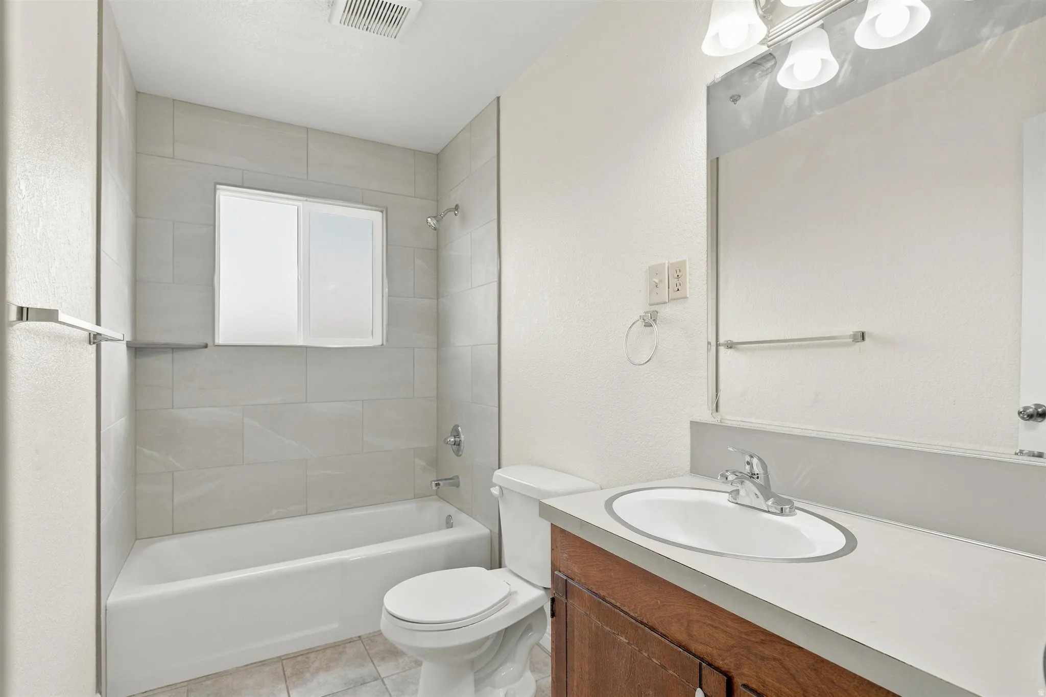 Bathroom featuring a white bathtub, light tile surround, and a vanity with a white countertop and wood-finish cabinetry