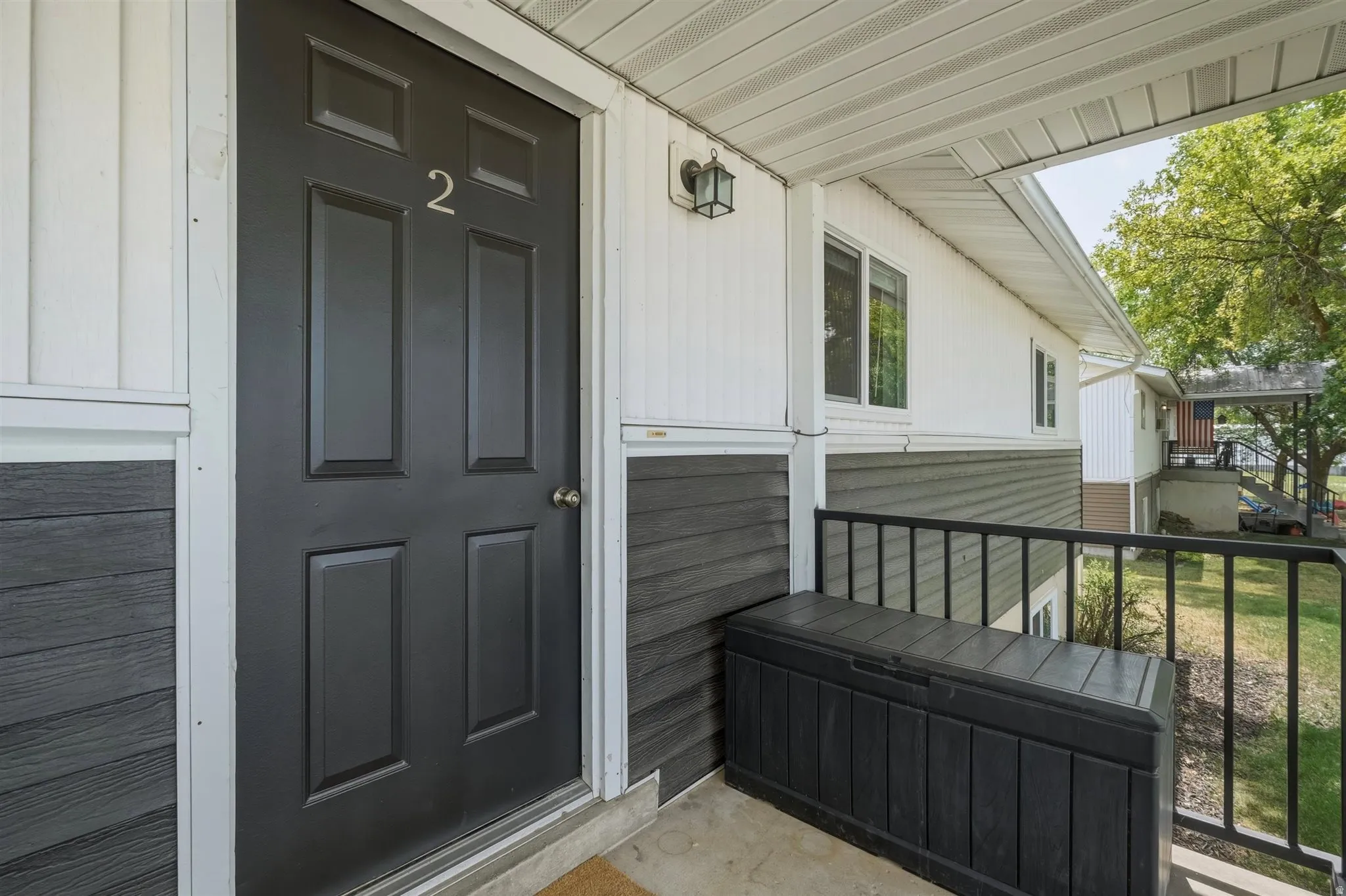 Exterior entrance featuring a paneled door, horizontal siding, vertical siding, an outdoor wall sconce, and a black metal railing