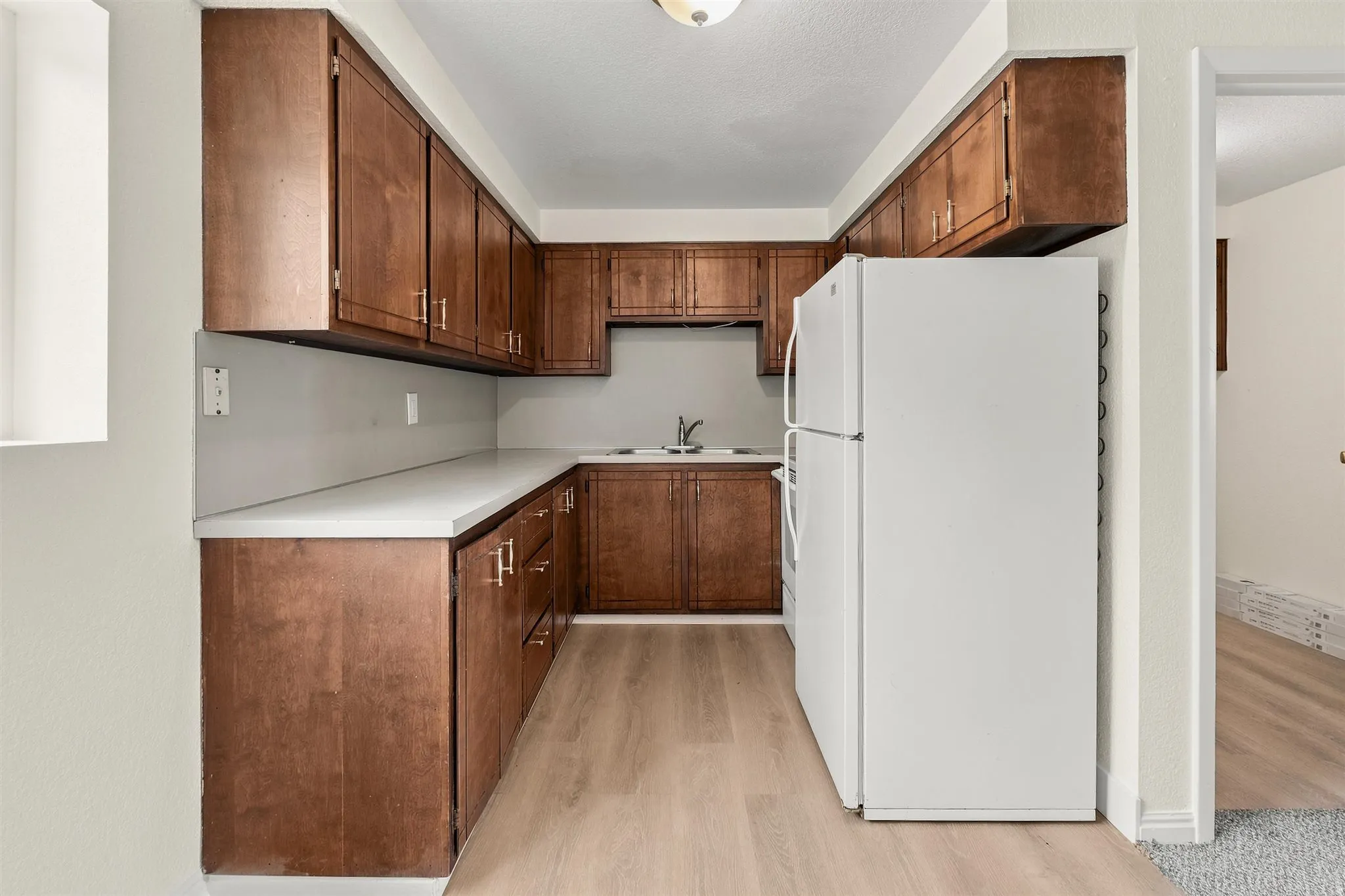 Compact kitchen featuring extensive wood-finish cabinetry, light-toned countertops, and wood-finish flooring