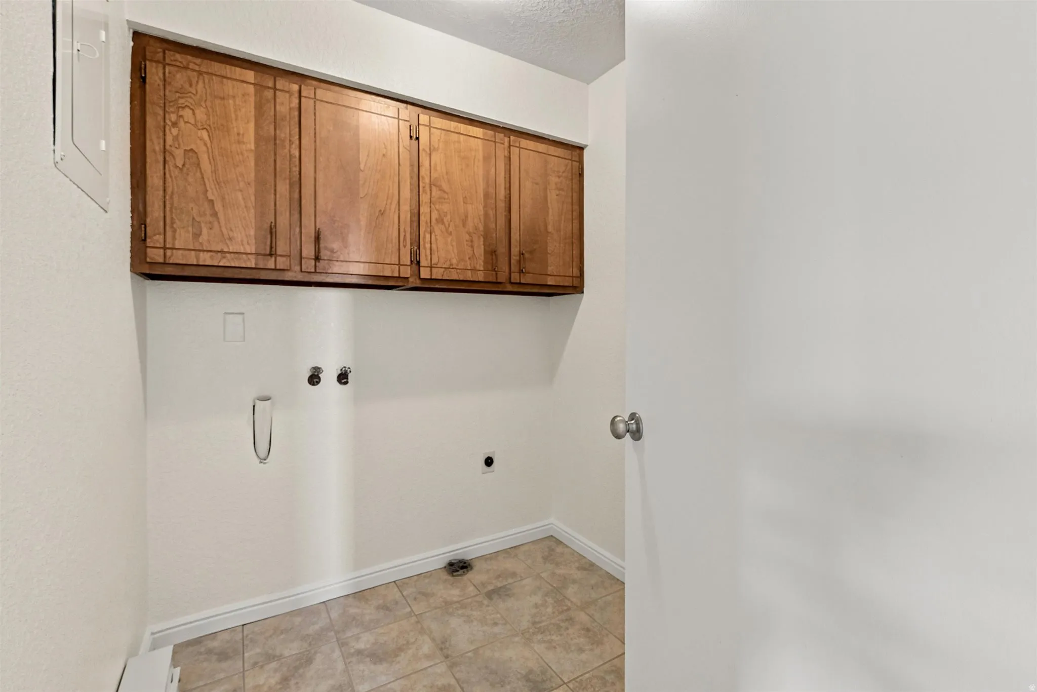 Utility space featuring upper wood cabinetry, neutral-toned tile flooring, and white baseboards