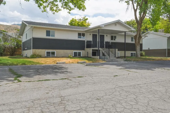 Two-story multi-unit structure featuring a covered entry porch, dark siding accents, and a paved parking area