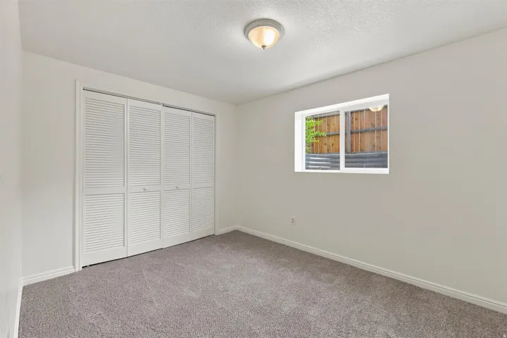 Interior room with neutral wall paint, gray carpet flooring, a flush-mount ceiling light, white louvered bifold closet doors, and a single window