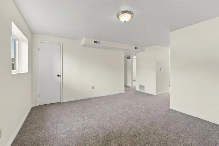 Spacious room featuring gray carpet, light-toned walls, a semi-flush mount ceiling light, and a window providing natural illumination