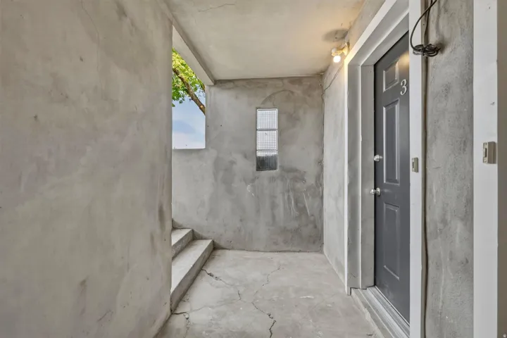 Entryway featuring a paneled door with a numeric plaque, concrete flooring, and a small rectangular window
