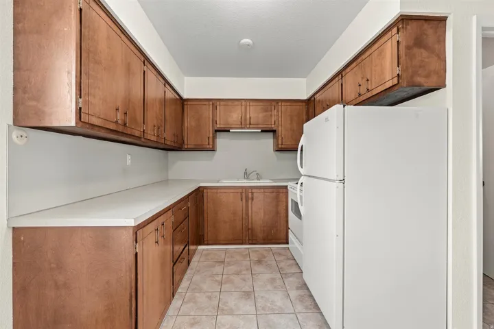 Kitchen featuring wood-finish cabinetry, white countertops, a white refrigerator, a white range, and tiled flooring