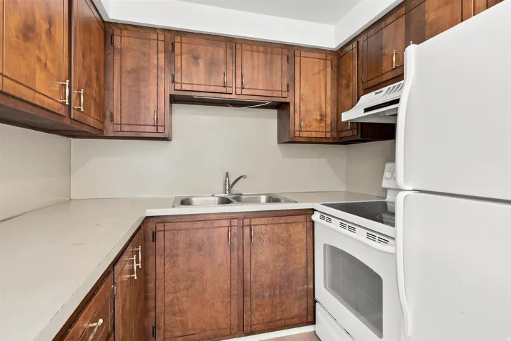 Kitchen featuring ample wood cabinetry, light-toned countertops, a stainless steel double-basin sink, white electric range with hood, and a white refrigerator