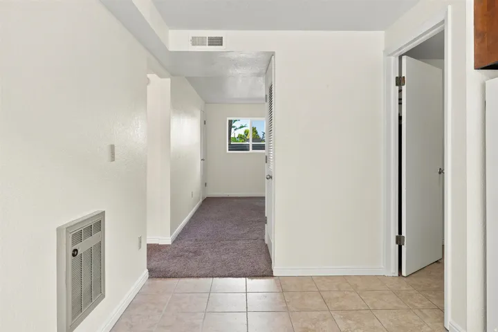 Interior hallway featuring light-toned tile flooring, neutral wall paint, and a wall-mounted ventilation unit