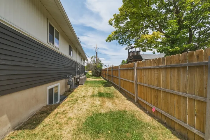 Side yard featuring a wooden privacy fence, a natural grass area, and a tree providing shade